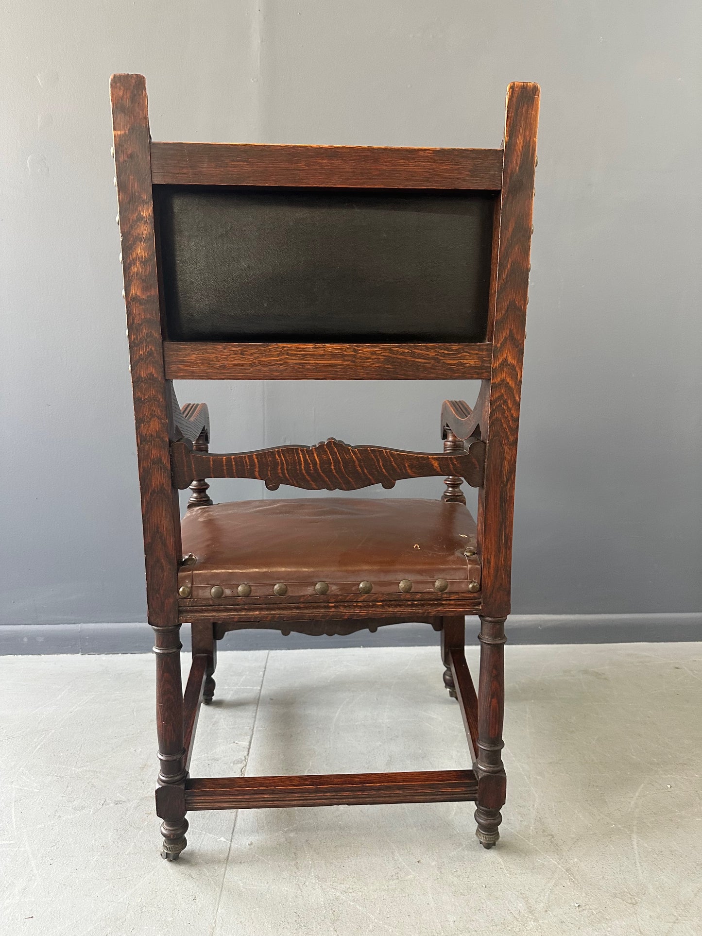 Impressive English 18th-century oak carved armchair featuring tooled leather backrest with heraldic motif, nailhead trim, and ornate turned wood detailing