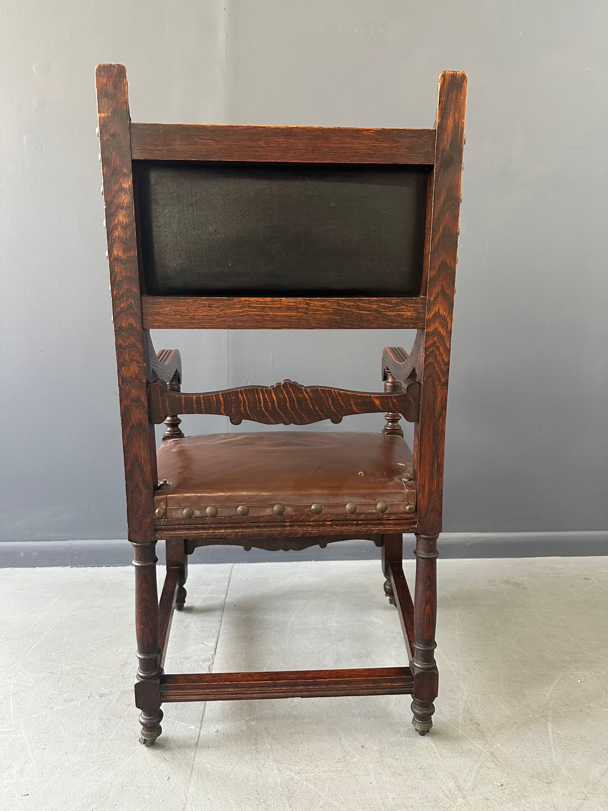 Impressive English 18th-century oak carved armchair featuring tooled leather backrest with heraldic motif, nailhead trim, and ornate turned wood detailing