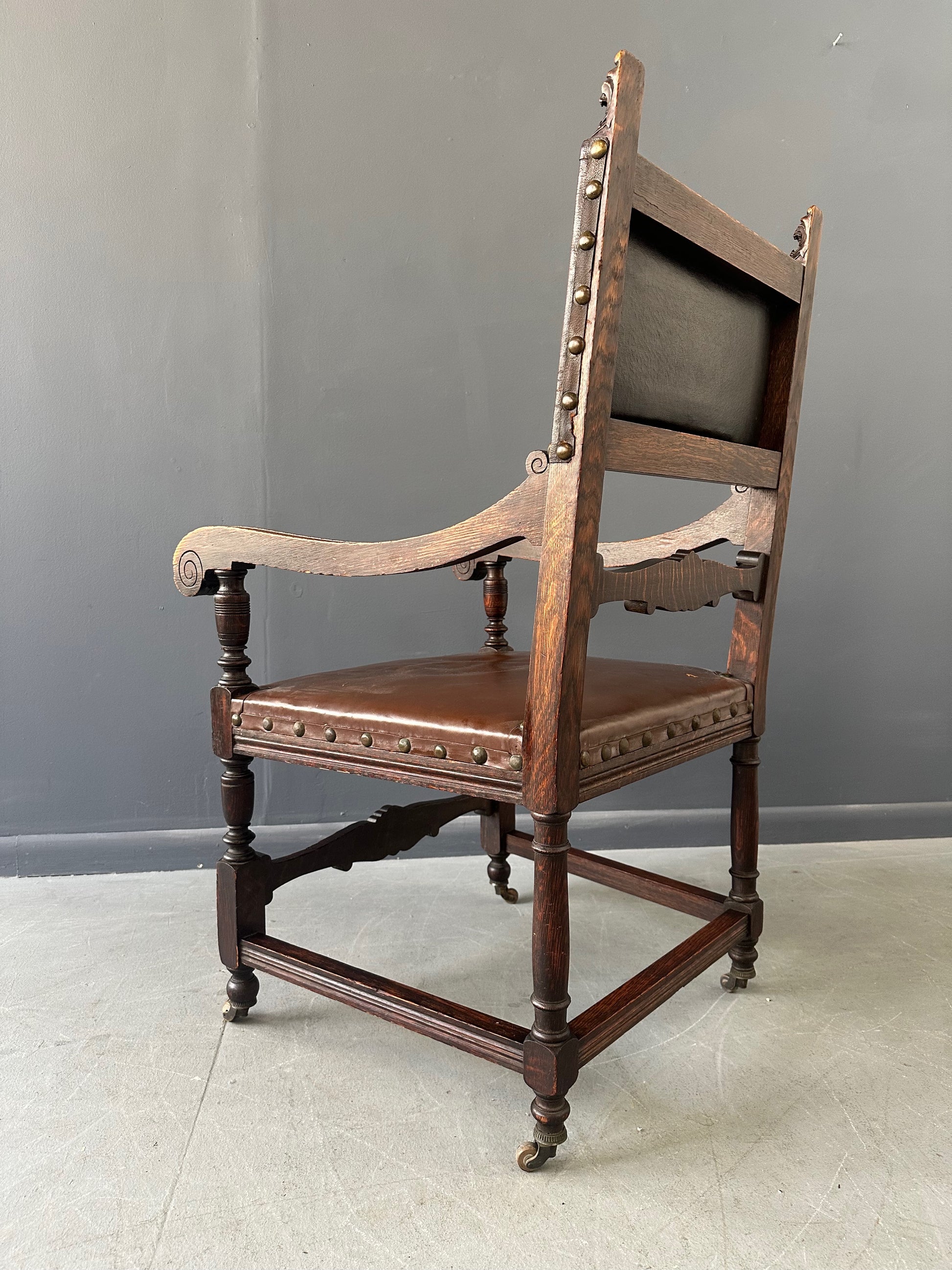 Impressive English 18th-century oak carved armchair featuring tooled leather backrest with heraldic motif, nailhead trim, and ornate turned wood detailing