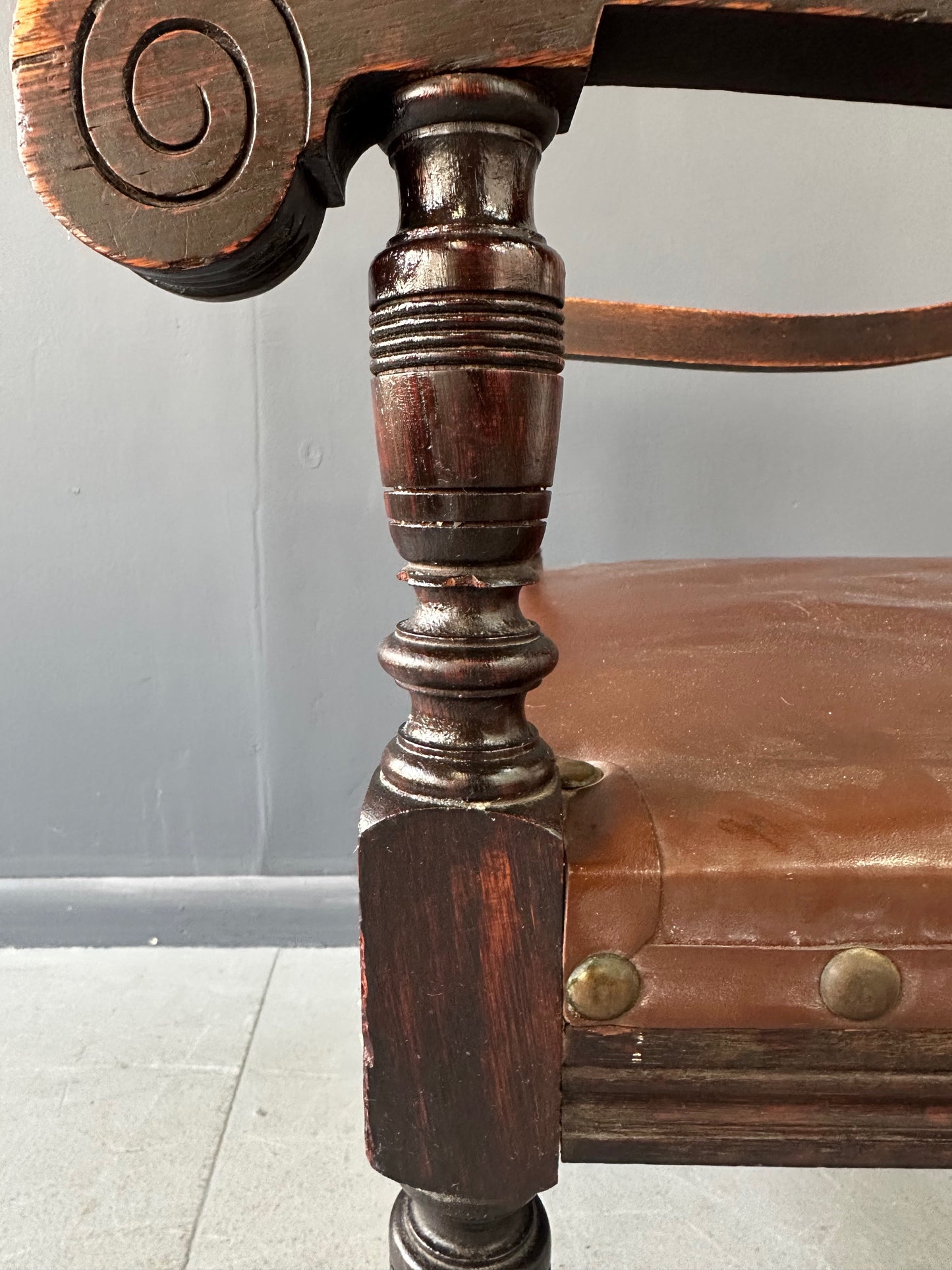 Impressive English 18th-century oak carved armchair featuring tooled leather backrest with heraldic motif, nailhead trim, and ornate turned wood detailing