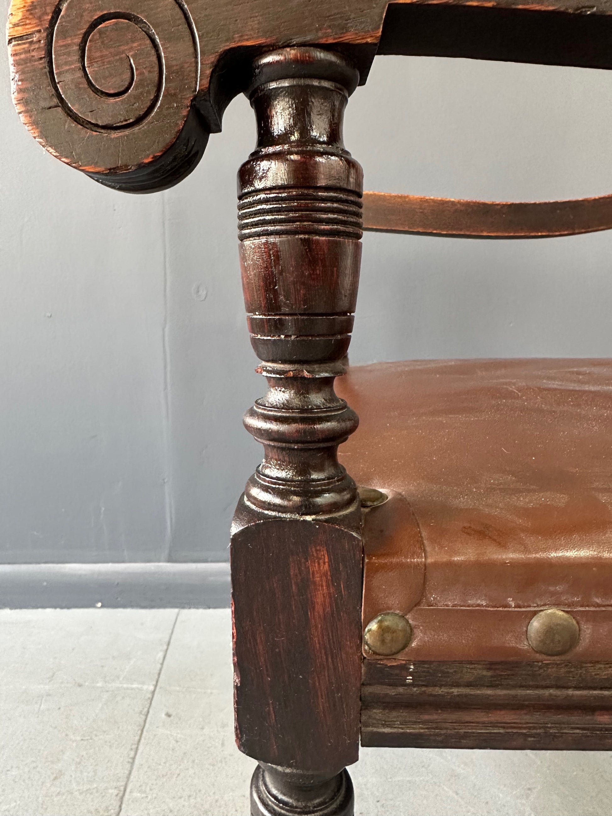 Impressive English 18th-century oak carved armchair featuring tooled leather backrest with heraldic motif, nailhead trim, and ornate turned wood detailing
