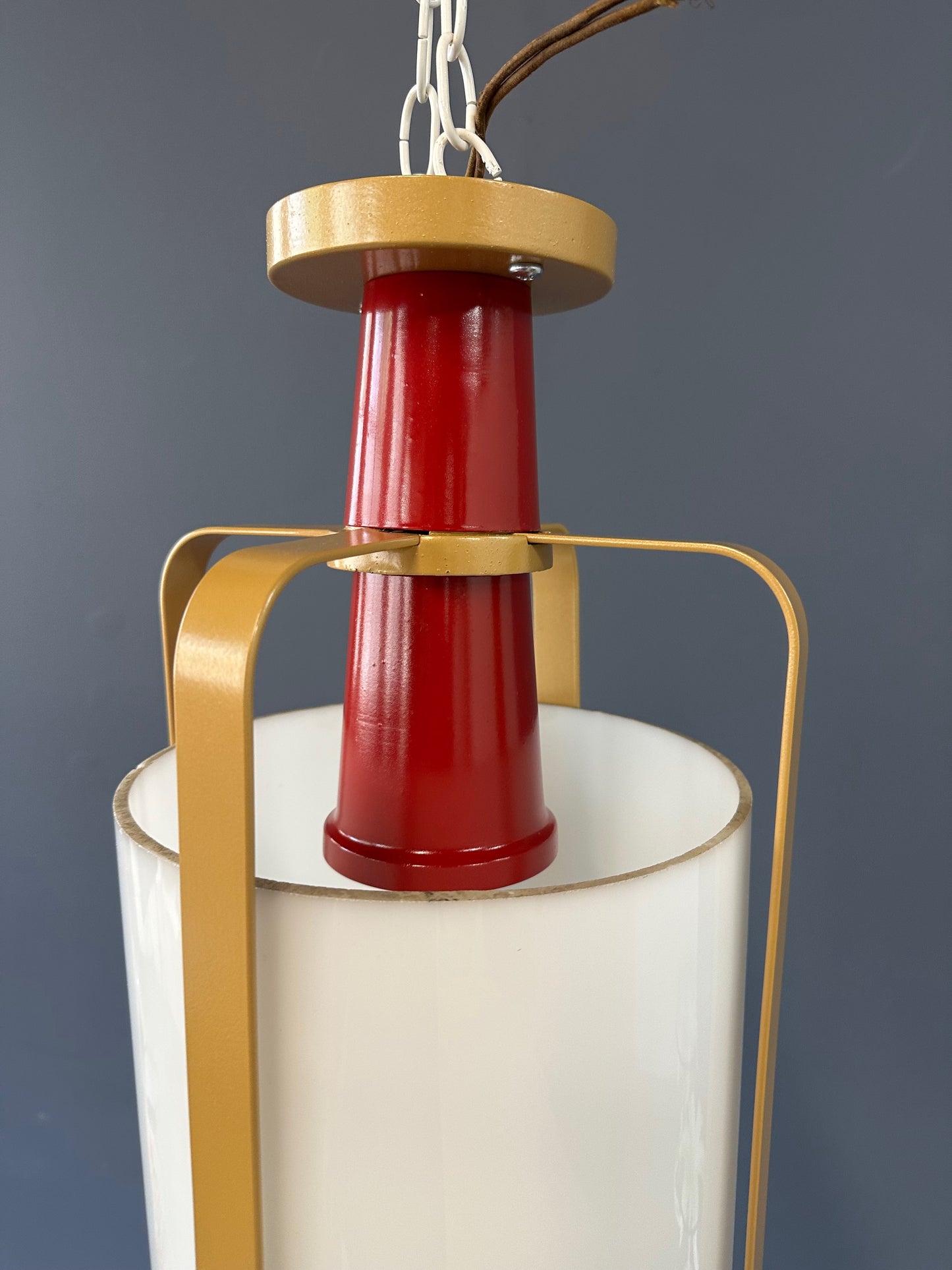 Pair of large pendant lights featuring cylindrical white glass shades encased in red and brass-colored metal frames, suspended by chains for ceiling mounting