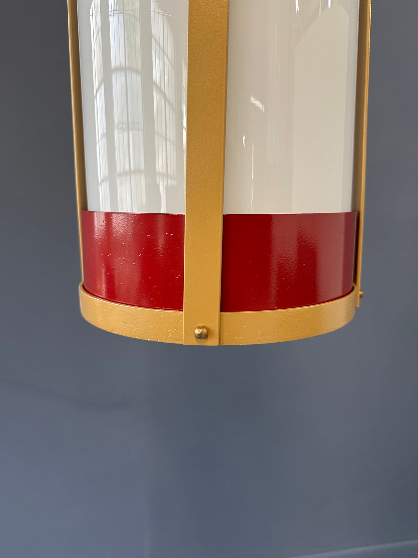 Pair of large pendant lights featuring cylindrical white glass shades encased in red and brass-colored metal frames, suspended by chains for ceiling mounting