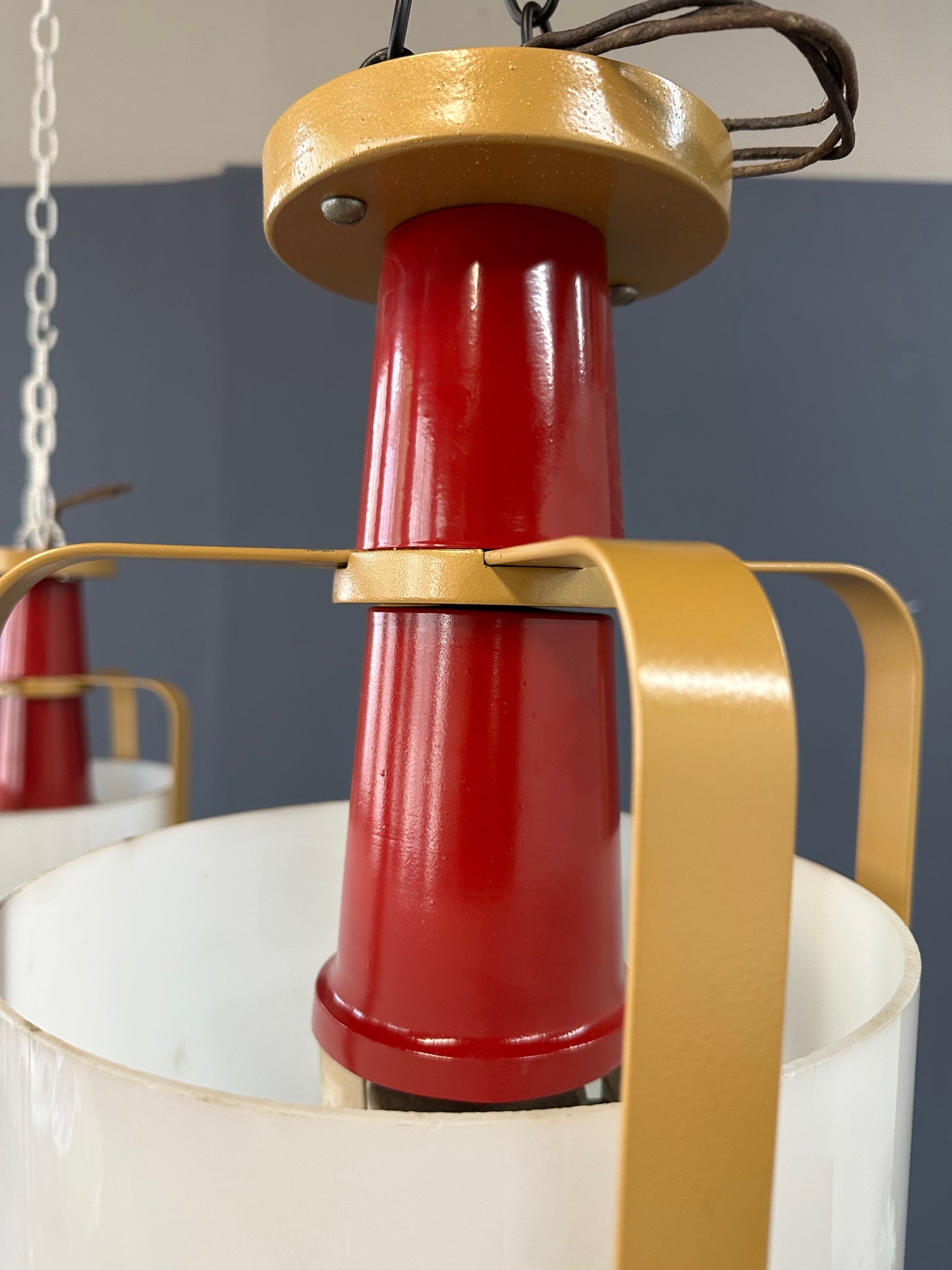 Pair of large pendant lights featuring cylindrical white glass shades encased in red and brass-colored metal frames, suspended by chains for ceiling mounting