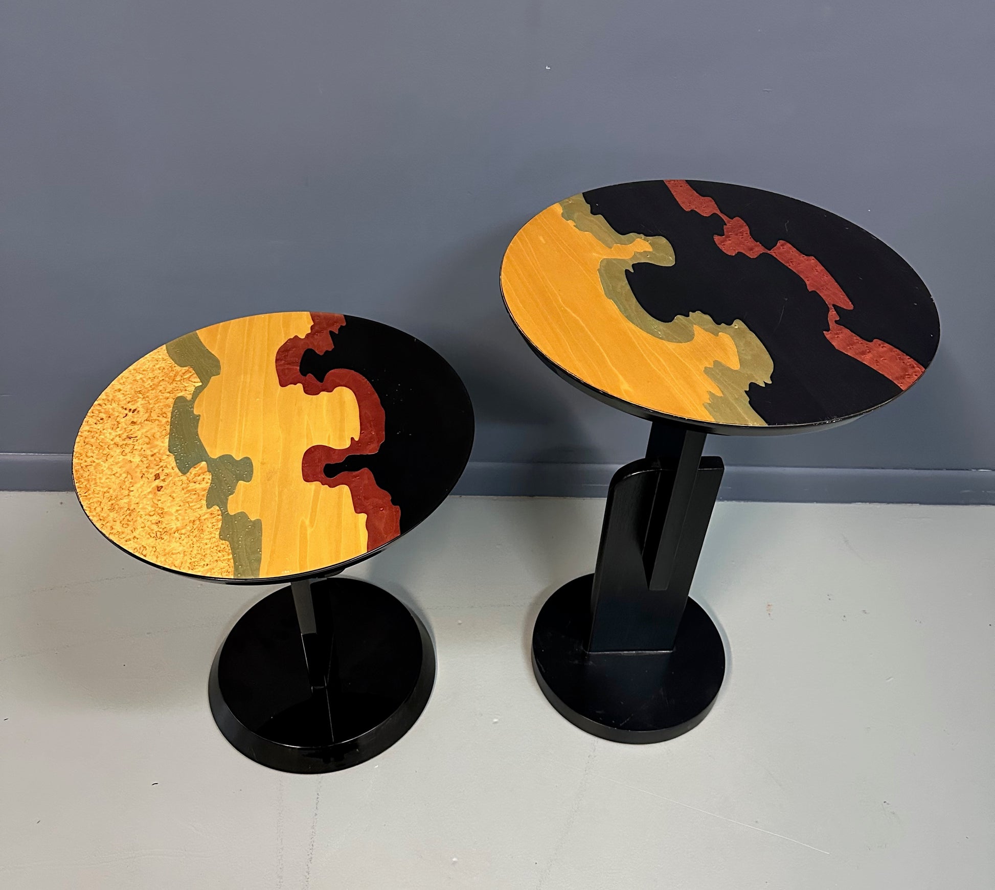 Pair of Carlo Malnati style Postmodern side tables featuring round inlaid wood tops with abstract, multicolored organic patterns and sleek black pedestal bases.