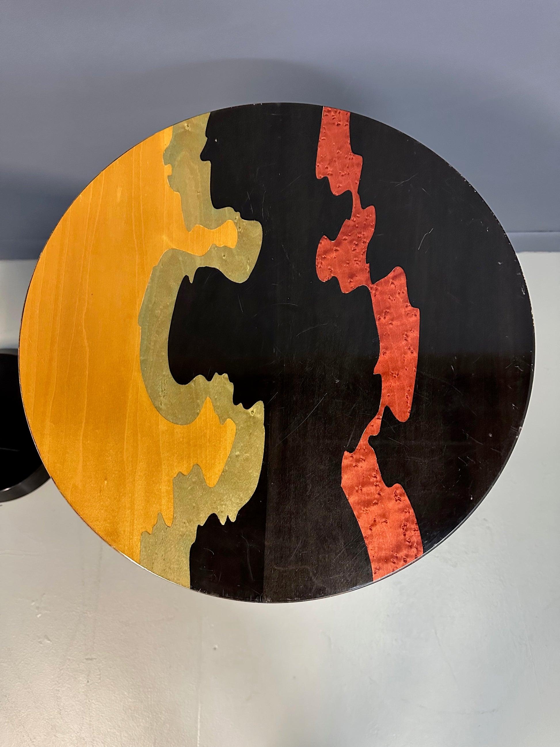 Pair of Carlo Malnati style Postmodern side tables featuring round inlaid wood tops with abstract, multicolored organic patterns and sleek black pedestal bases.