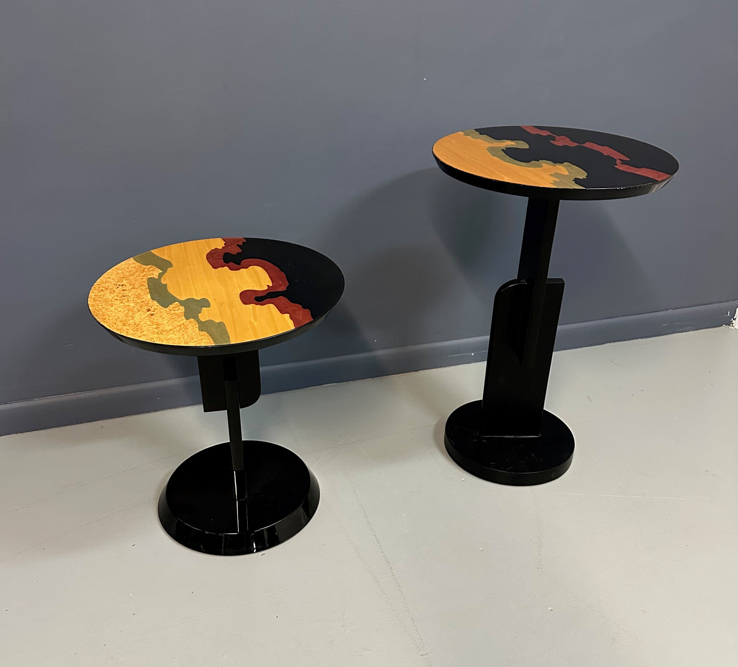 Pair of Carlo Malnati style Postmodern side tables featuring round inlaid wood tops with abstract, multicolored organic patterns and sleek black pedestal bases.