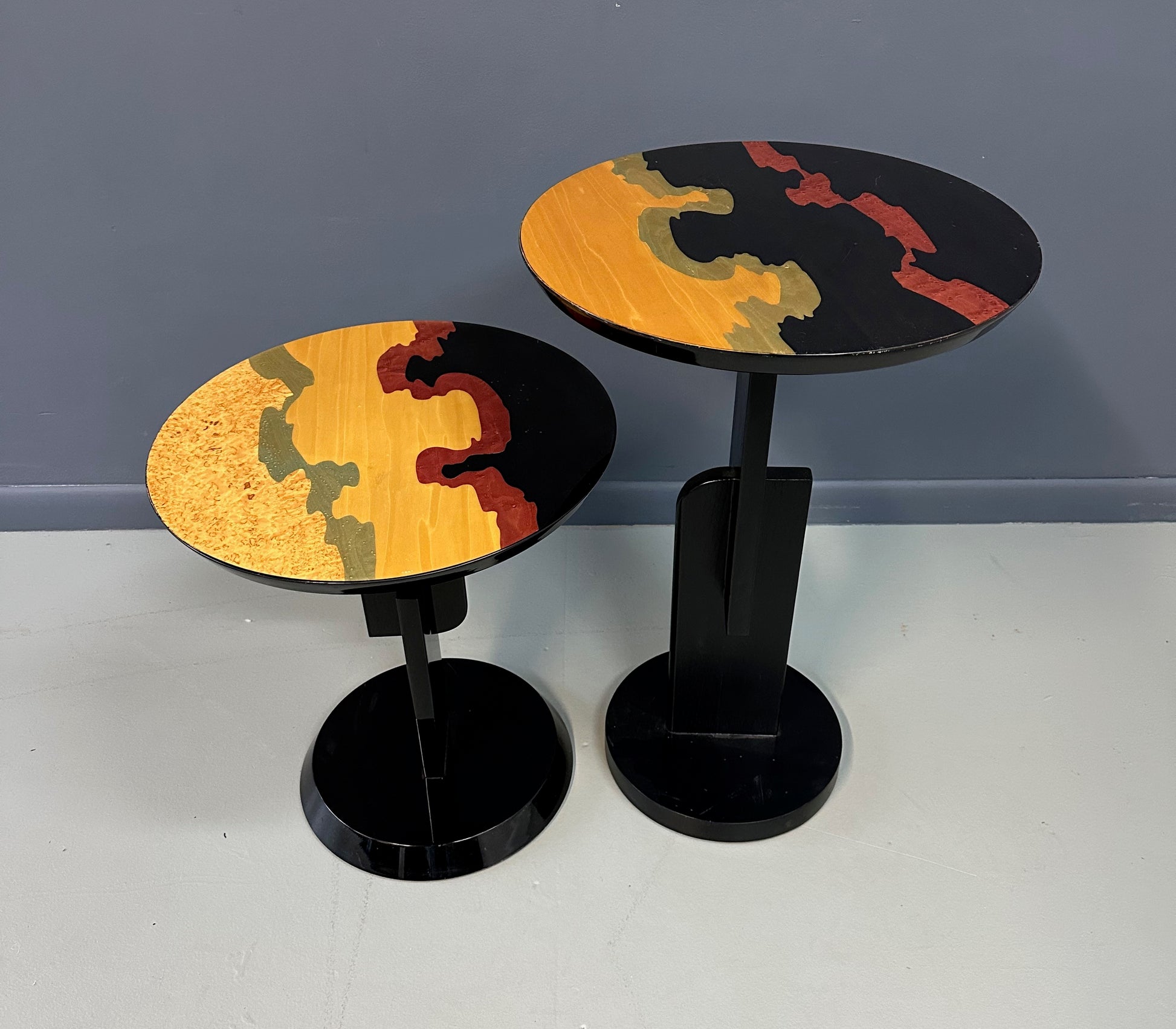 Pair of Carlo Malnati style Postmodern side tables featuring round inlaid wood tops with abstract, multicolored organic patterns and sleek black pedestal bases.