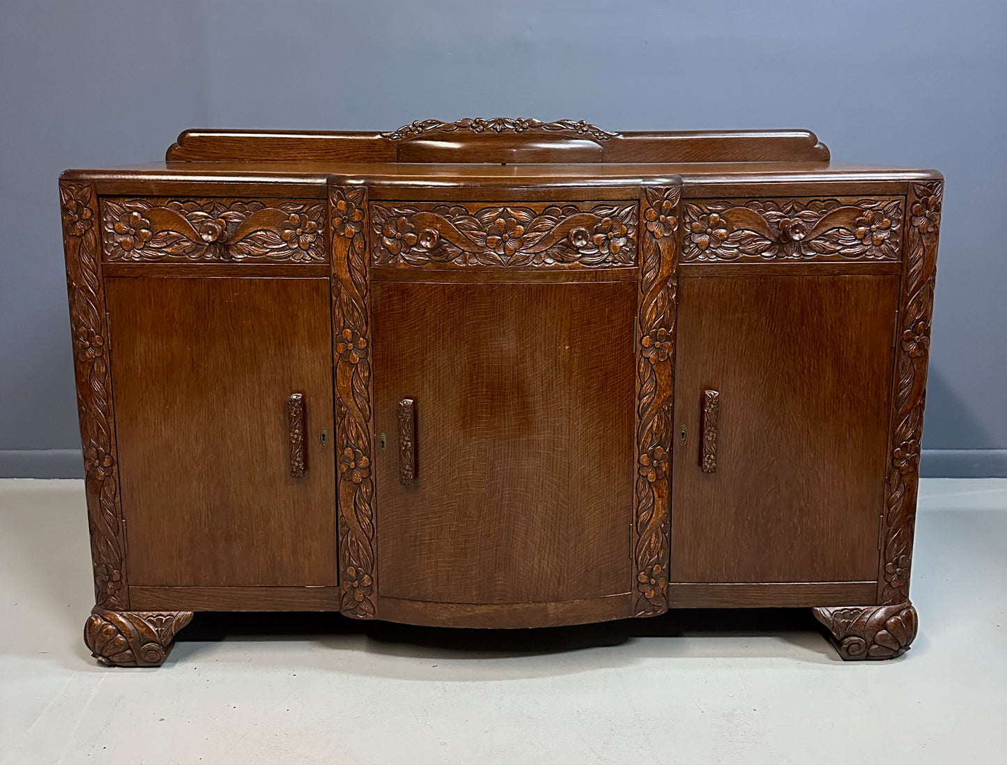 1920s English Art Nouveau sideboard in oak with ornate floral and vine hand-carving, three-door storage, and bun feet