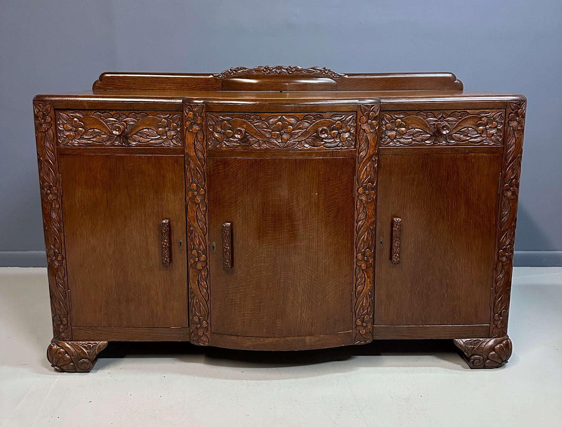 1920s English Art Nouveau sideboard in oak with ornate floral and vine hand-carving, three-door storage, and bun feet