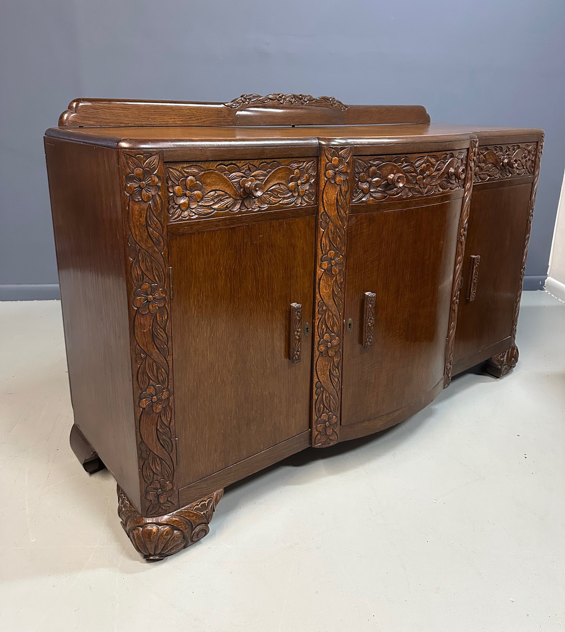 1920s English Art Nouveau sideboard in oak with ornate floral and vine hand-carving, three-door storage, and bun feet