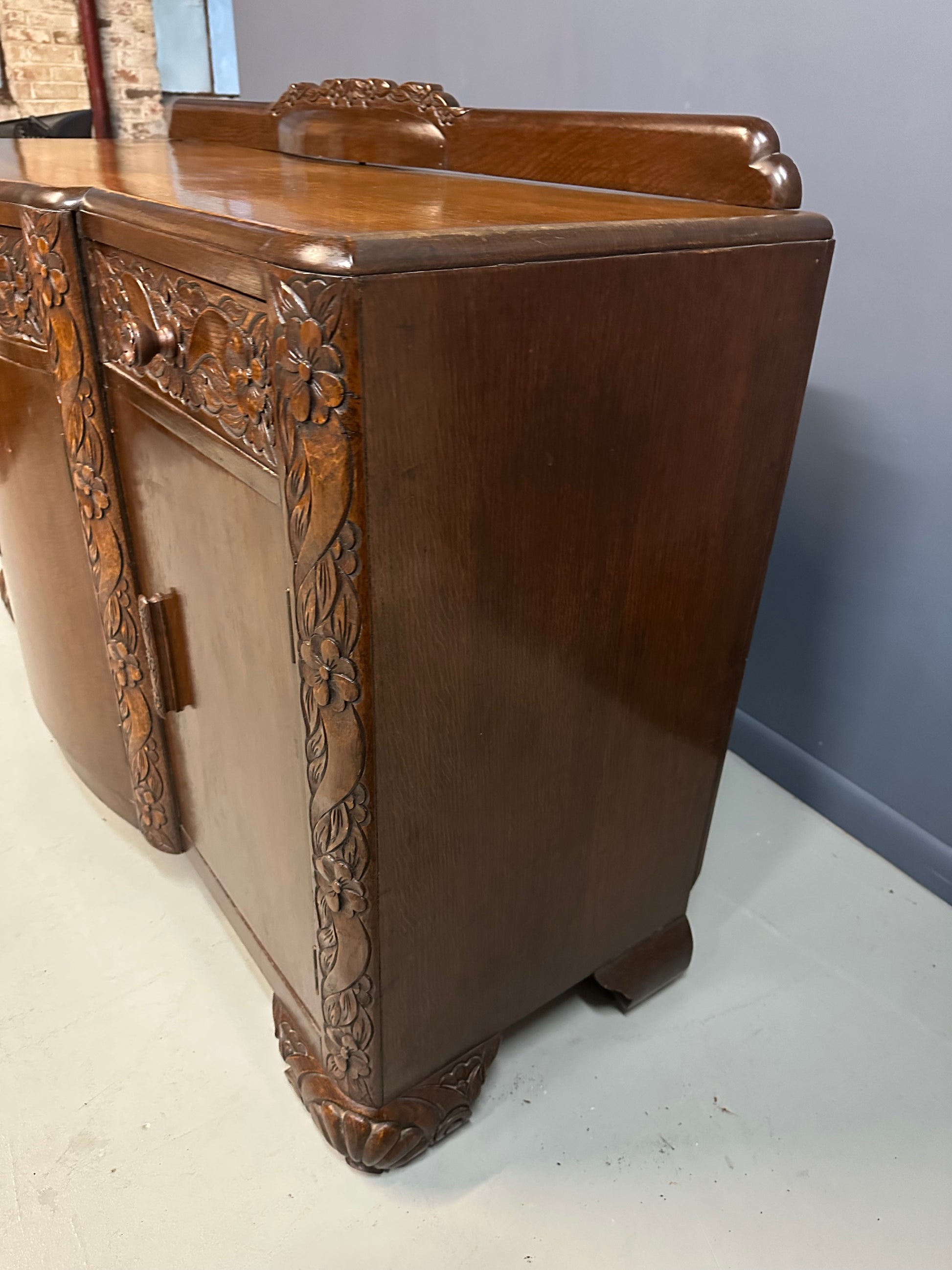 1920s English Art Nouveau sideboard in oak with ornate floral and vine hand-carving, three-door storage, and bun feet