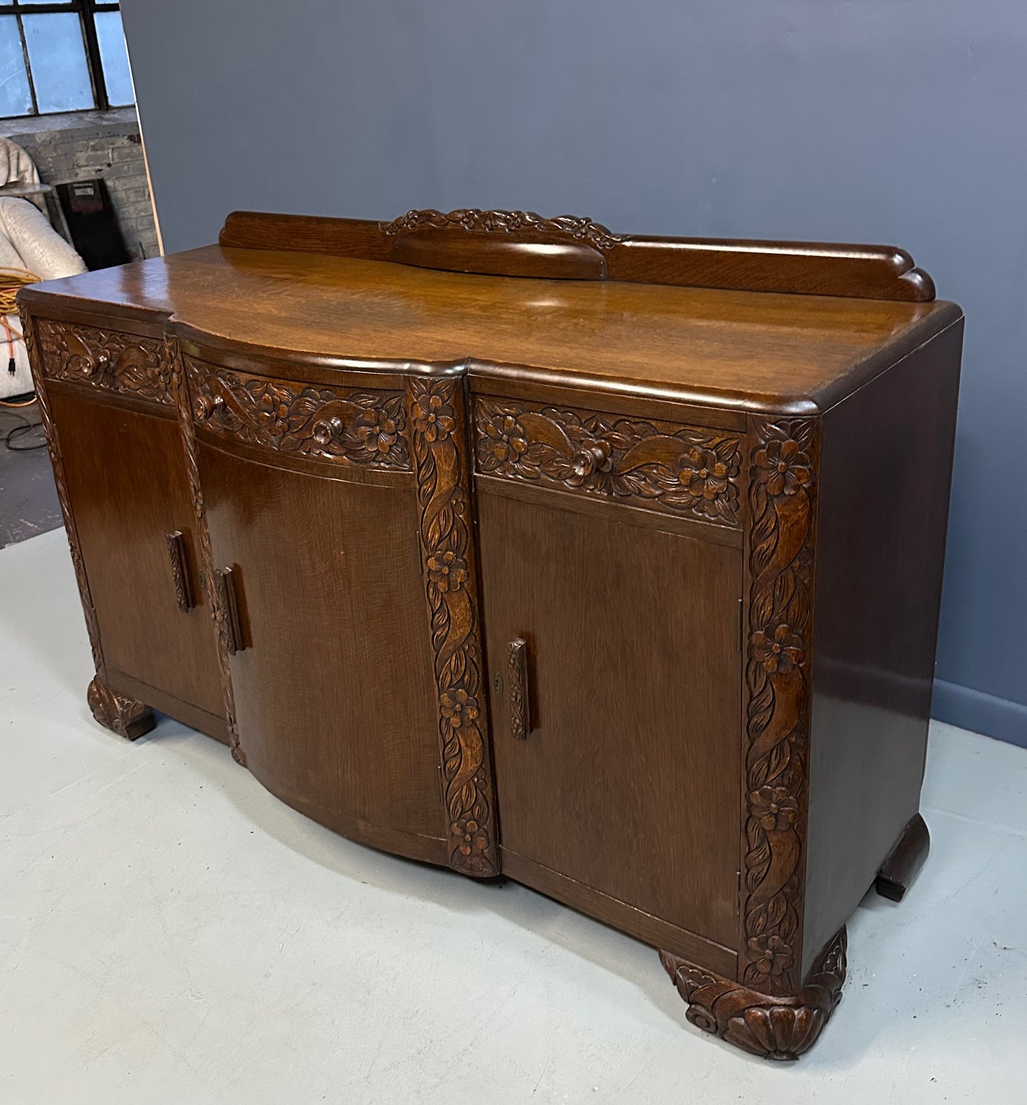 1920s English Art Nouveau sideboard in oak with ornate floral and vine hand-carving, three-door storage, and bun feet