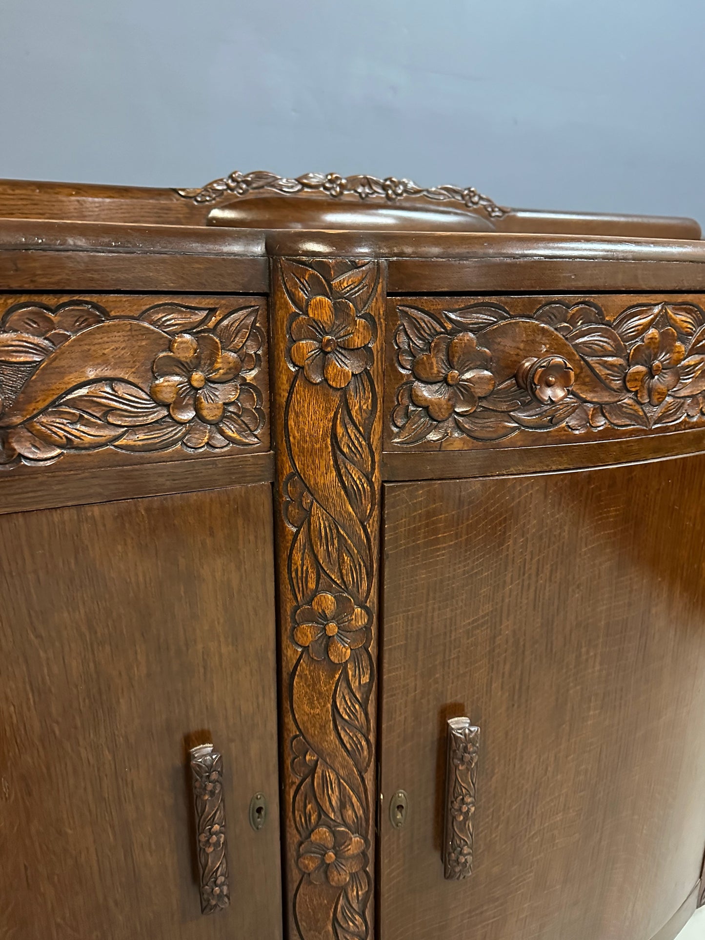 1920s English Art Nouveau sideboard in oak with ornate floral and vine hand-carving, three-door storage, and bun feet