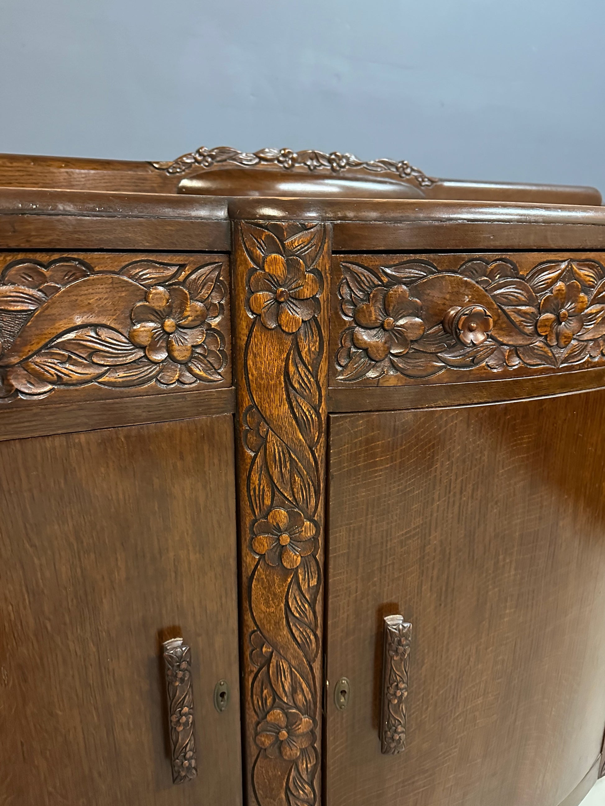 1920s English Art Nouveau sideboard in oak with ornate floral and vine hand-carving, three-door storage, and bun feet