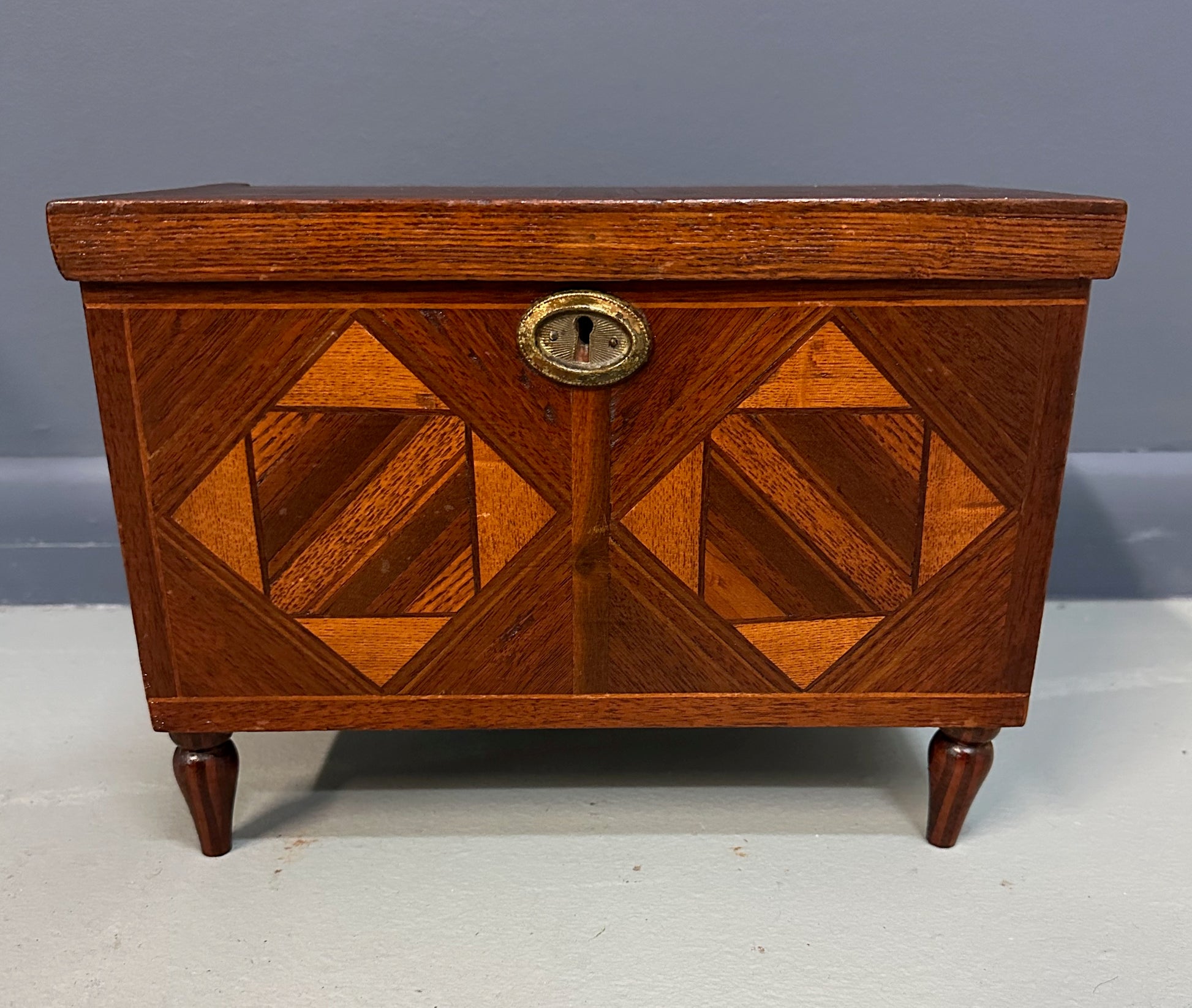 Miniature marquetry blanket chest dated 1910, handcrafted by Flora Boyer of Pennsylvania, featuring intricate geometric inlay patterns in warm-toned wood and a brass keyhole on the front
