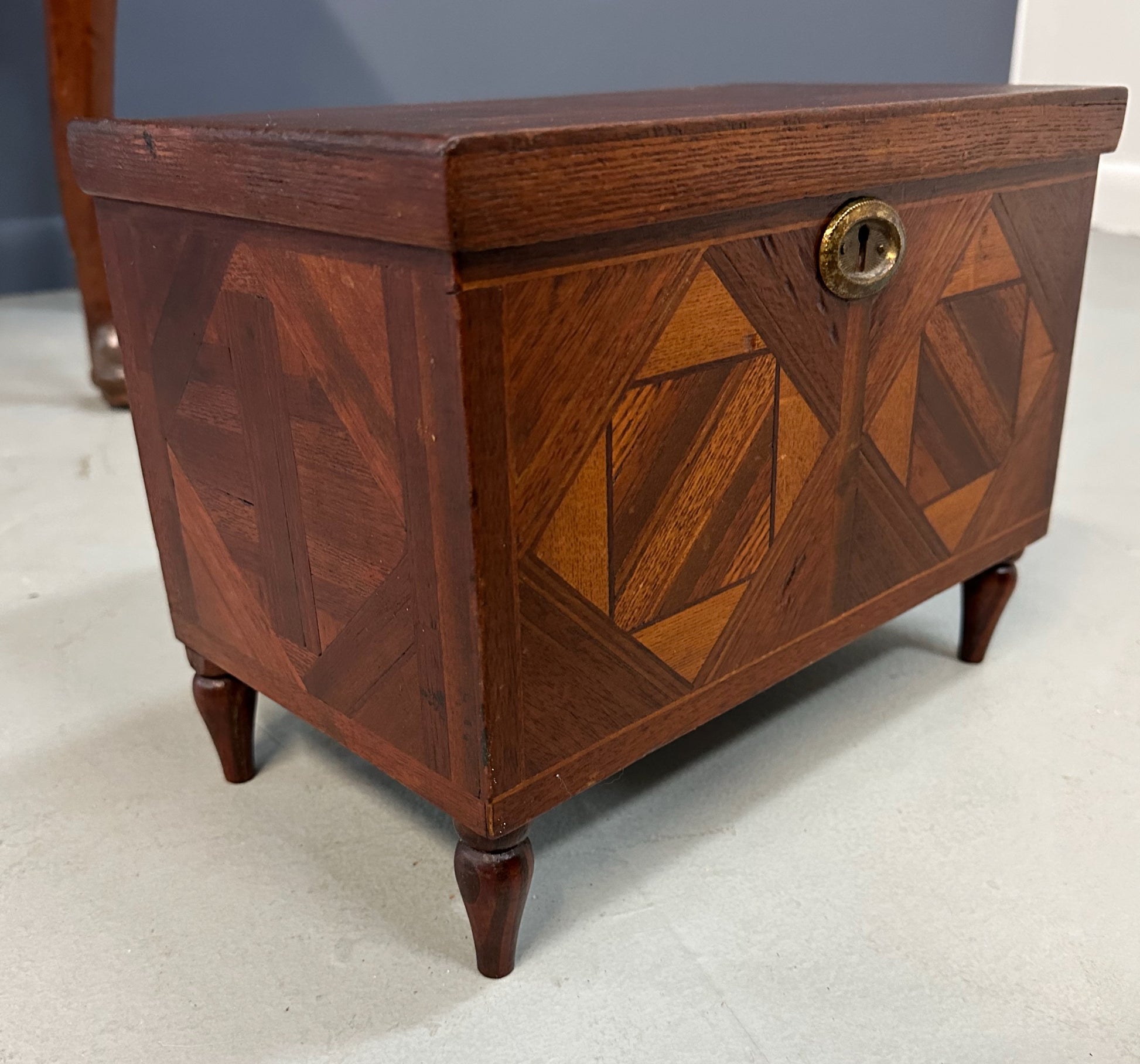 Miniature marquetry blanket chest dated 1910, handcrafted by Flora Boyer of Pennsylvania, featuring intricate geometric inlay patterns in warm-toned wood and a brass keyhole on the front