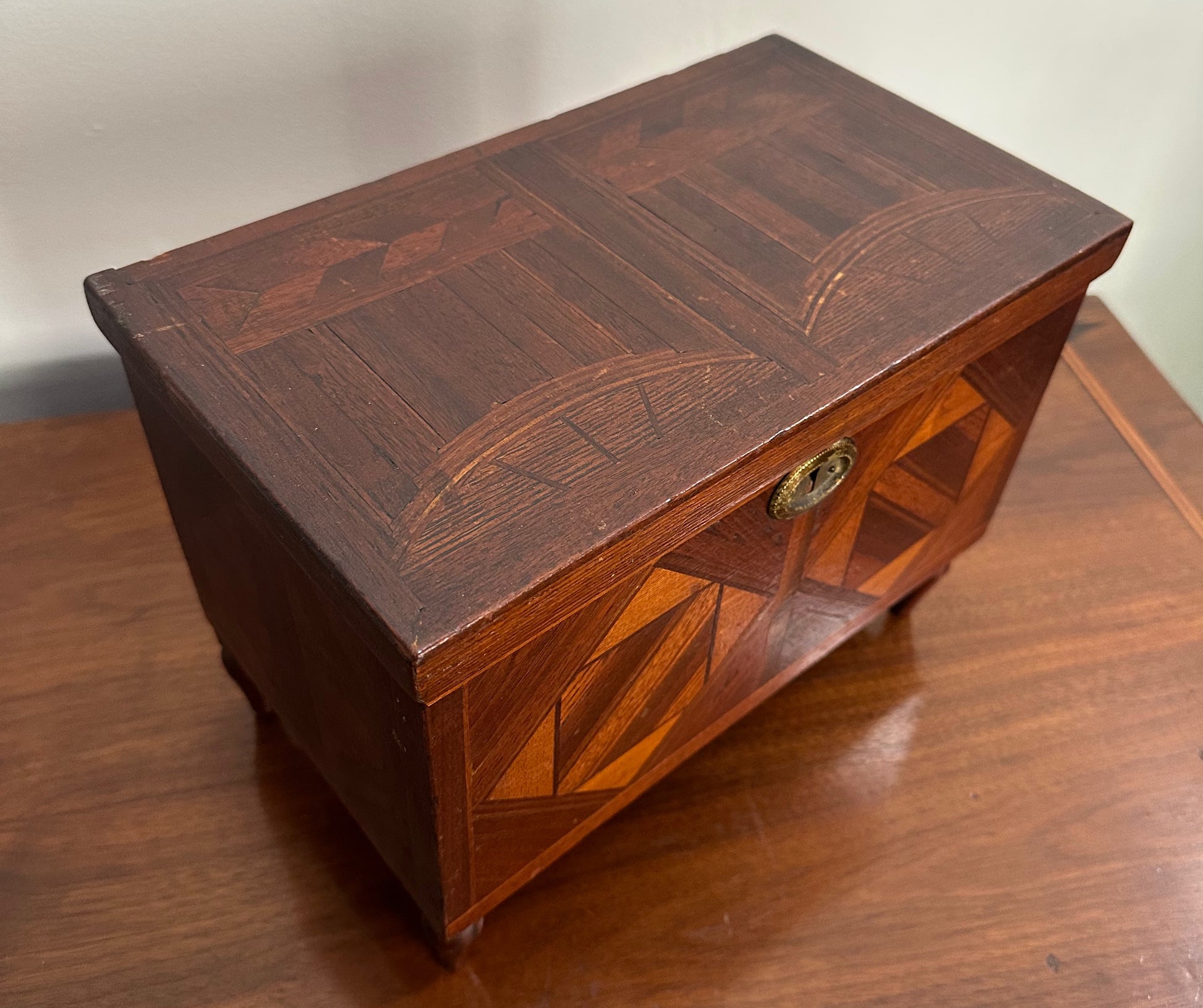 Miniature marquetry blanket chest dated 1910, handcrafted by Flora Boyer of Pennsylvania, featuring intricate geometric inlay patterns in warm-toned wood and a brass keyhole on the front