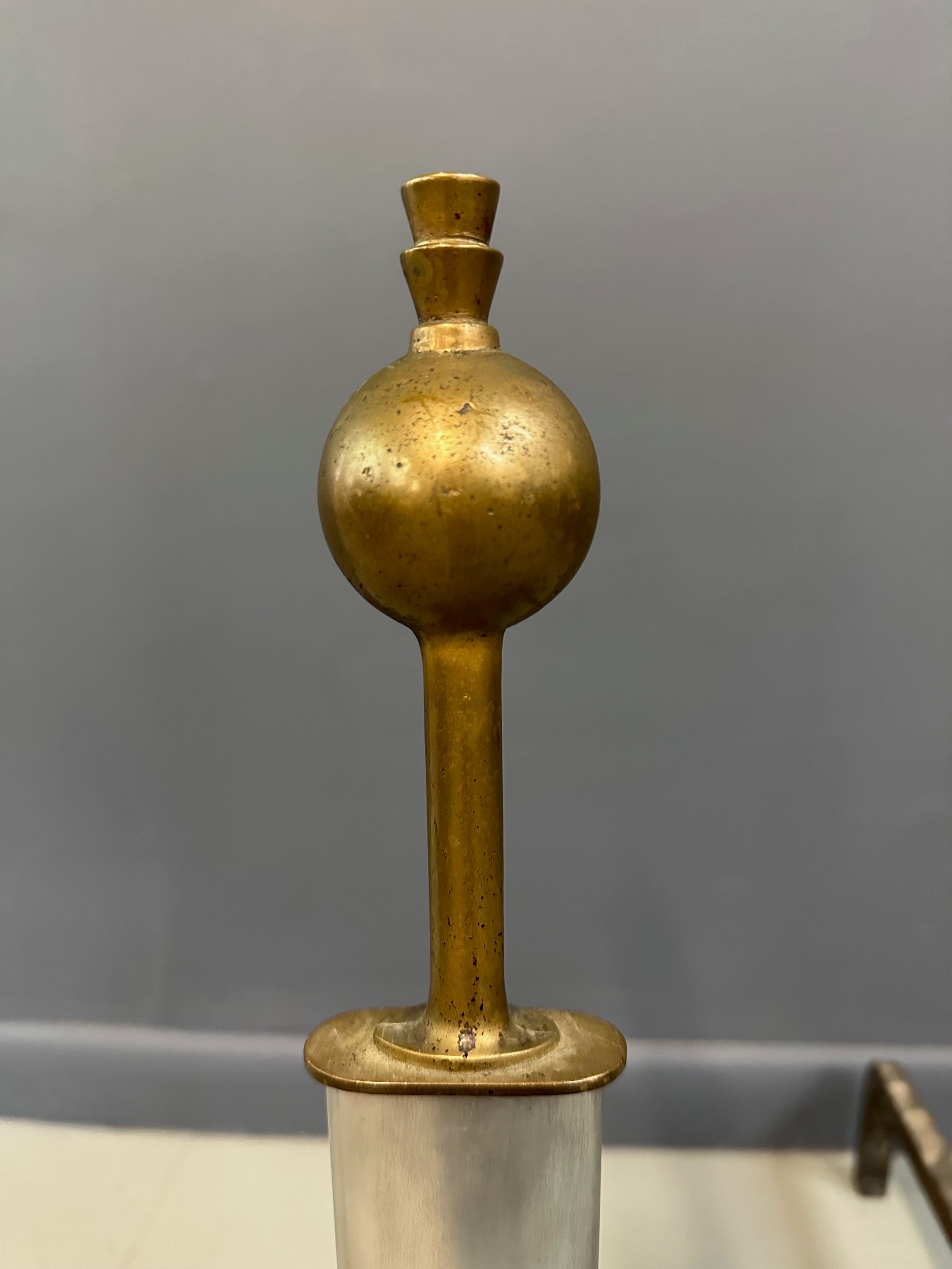 Pair of Machine Age andirons made of polished steel columns with spherical brass finials on top, supported by rugged iron bases with a minimalist, industrial design.