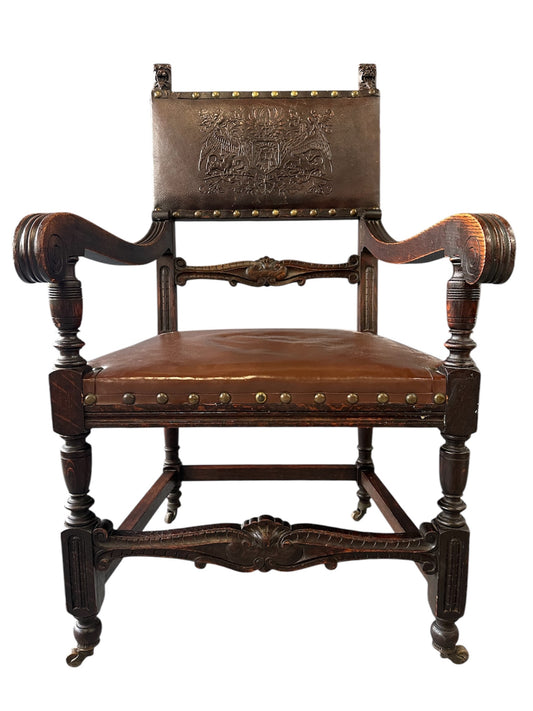 Impressive English 18th-century oak carved armchair featuring tooled leather backrest with heraldic motif, nailhead trim, and ornate turned wood detailing