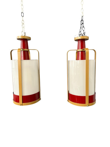Pair of large pendant lights featuring cylindrical white glass shades encased in red and brass-colored metal frames, suspended by chains for ceiling mounting