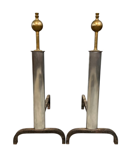 Pair of Machine Age andirons made of polished steel columns with spherical brass finials on top, supported by rugged iron bases with a minimalist, industrial design.